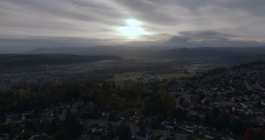 Aerial view of a suburban neighborhood with sunrise breaking through cloudy skies, Mount Rainier in the distance, Pacific Northwest, Washington State, USA.
