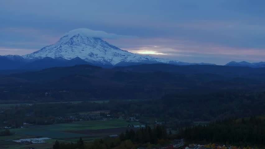 Aerial view of Mount Rainier at sunrise with snow-covered peak, distant mountains, and early morning sky, Pacific Northwest, Washington State, USA.