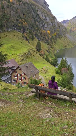 Nestled in the Swiss Alps, a person relaxes on a bench overlooking a lake, surrounded by majestic mountains and autumn foliage. Falensee lake Alps mountains, Appenzell Innerrhoden, Switzerland.