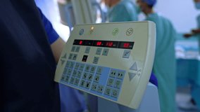Female medic stands at the control panel of the C-Arm x-ray machine. Group of four doctors work at operating table. - Powered by Shutterstock - Get 15% off with code: PIKWIZARD15