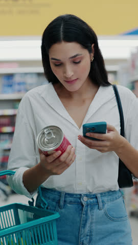 Vertical Video. Pretty Lady On A Calorie Conscious Diet Analyzes Can Contents And Noting Nutritional Information Into Her Smartphone. Female Reading the Content of the Product. Shopping Concept