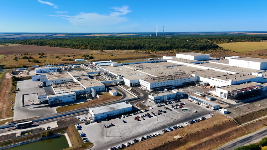 Low-rise premises of a huge industrial plant locating in the fields. Car park with automobiles at the factory. Top view.
