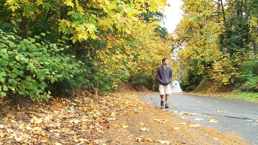 Model released man walks up street full of autumn leaves.
