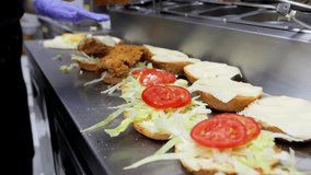 A close-up of a cook making burgers in a fast food restaurant, placing fried meat on a bun with vegetables. The burger-making process and fast food cooking concept. - Powered by Shutterstock - Get 15% off with code: PIKWIZARD15