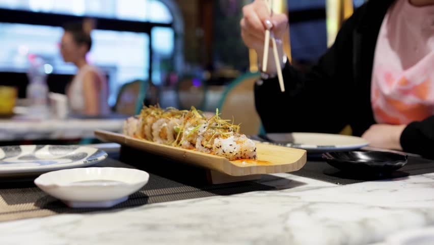 A woman enjoys sushi using chopsticks in a Japanese restaurant, highlighting the experience of traditional Japanese cuisine.