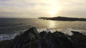 Watch the stunning sunset casting golden hues over the ocean waves as they crash against rugged coastal cliffs. Distant islands are visible in this picturesque setting. - Powered by Shutterstock - Get 15% off with code: PIKWIZARD15
