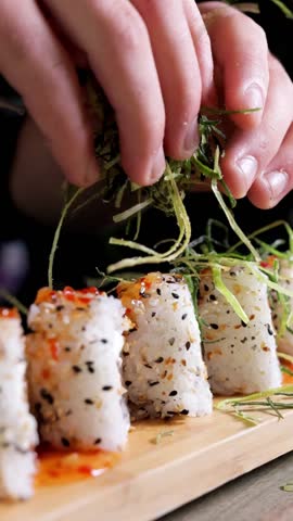 A chef’s hands lay thinly sliced seaweed on sushi rolls in slow motion. Vertical video format, ideal for Japanese food preparation, sushi, and cooking-related content.