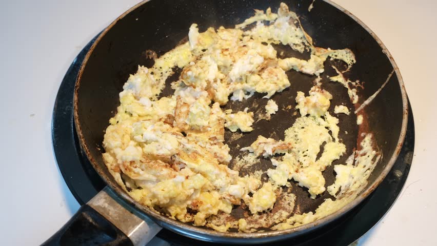 Scrambling eggs in frying pan with a fork. Top view. No people.