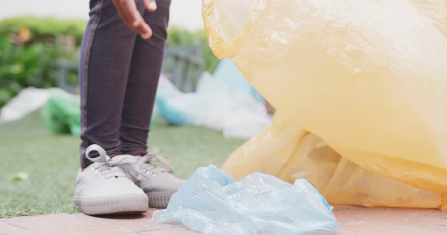 Video of low section of biracial schoolgirl collecting recycling in schoolyard, copy space. Education, childhood, inclusivity, ecology, elementary school and learning concept.