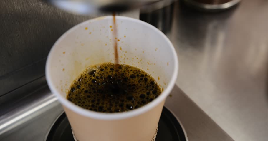 A close-up shot of freshly brewed coffee pouring into a paper cup from a professional coffee machine rich dark liquid flowing smoothly barista's craft cafe culture highlighting the brewing process