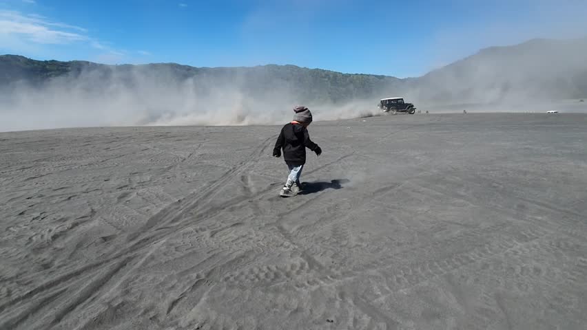 A small child runs in the sea of sand, passing jeeps in slow motion