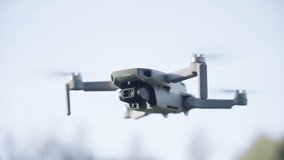 A small drone is flying in the sky. The drone is grey and has a camera on it. The sky is clear and blue - Powered by Shutterstock - Get 15% off with code: PIKWIZARD15
