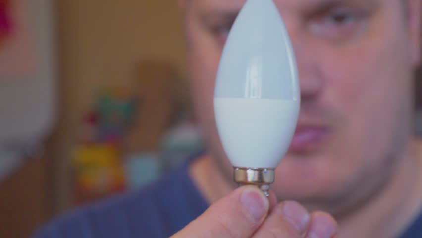 A middle-aged man carefully examines an electric lamp. Selective focus on the lamp and hands. Close-up. Shallow depth of field.