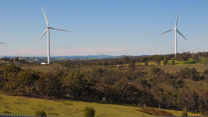 Aerial drone pullback reverse view of a hybrid solar and wind farm showing the large wind turbines for renewable clean energy supply located at Bannister in the Upper Lachlan Shire, NSW, Australia 