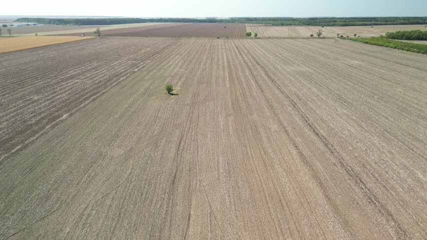 A drone flying above a farmland with a road seen in the distant background, on a sunny day