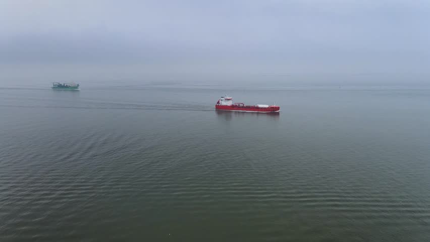 Drone footage of a red cargo ship navigating the North Sea near Cuxhaven, Germany, on a cloudy day. Video of the exposed seabed and vibrant vessel.