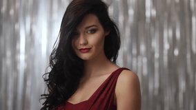 A glamorous woman with long dark hair poses in a red dress against a silver backdrop, exuding elegance and confidence. Portrait of a woman with long dark hair, posing against a shimmering silver - Powered by Shutterstock - Get 15% off with code: PIKWIZARD15