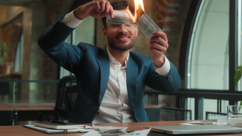 Indian Arabian male guy business man businessman crazy mad happy fooling laughing at office hold burning fake money trick joke waste cash enjoy burn paper banknotes finance excited rejoice have fun