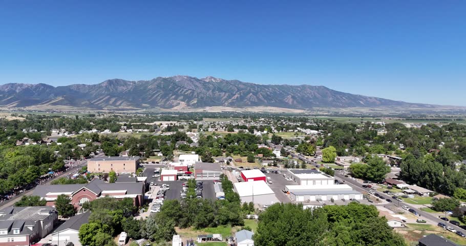 A drone flying above the houses of Utah town with green trees and mountain on a sunny day with blue sky