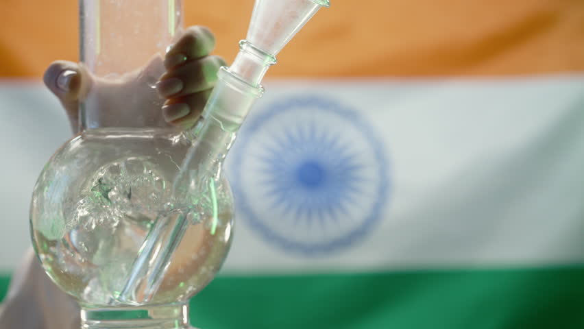 Woman smoking medical marijuana, glass water bong on indian flag background. Cannabis tobacco, Shisha in India