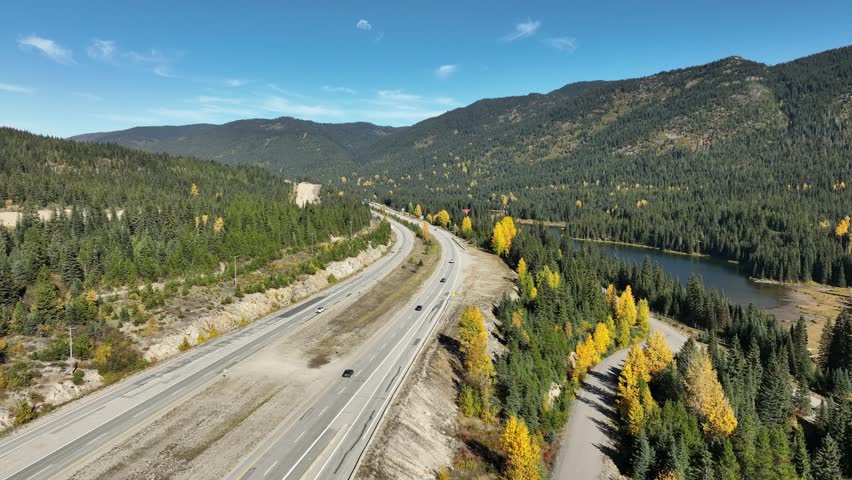A drone above Coquihalla Highway on a sunny day, near Coquihalla Lakes, surrounded by fall trees and mountains in British Columbia, Canada