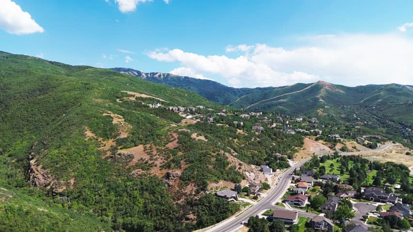 An aerial view of a mountain road surrounded by greenery and houses on a sunny day with blue sky