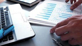 A business professional closely examines financial figures on a printed chart, with hands pointing to key data. A laptop, partially visible in the frame, adds to the modern office setting. - Powered by Shutterstock - Get 15% off with code: PIKWIZARD15