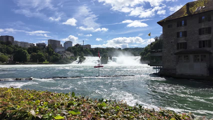 A boat sailing in the Rhine River near the Rhine Falls, on a sunny day surrounded by trees and buildings in Neuhausen town, Switzerland