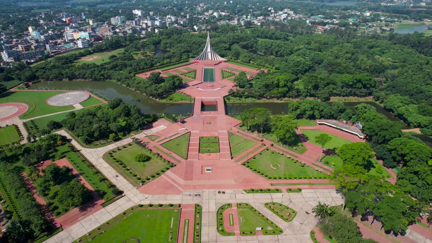 An aerial view of the National Martyrs Memorial of Bangladesh surrounded by vegetation, with city in the background in Dhaka