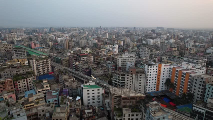 An aerial footage of Dhaka Metro Rail Train moving on a flyover rail track through a cement forest at sunset in Dhaka, Bangladesh