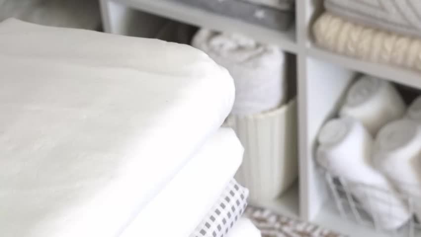 Hands put a branch of cotton on a clean white bed linen. Eco life concept. Background of a neat closet with linens.