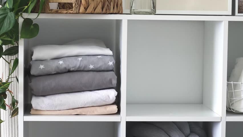 A woman neatly folds bed linen and towels in a closet in the bedroom. The concept of space organization and storage.