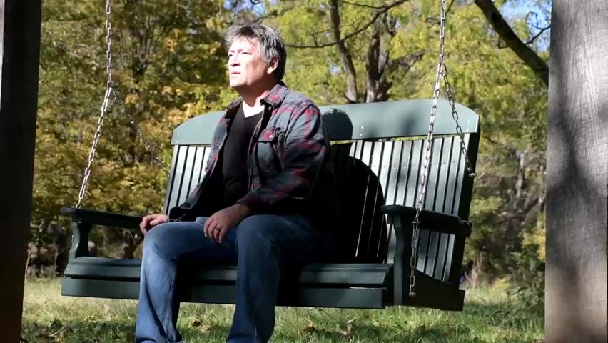 Concerned middle aged Caucasian  man rises from an outdoor swing and walks away.