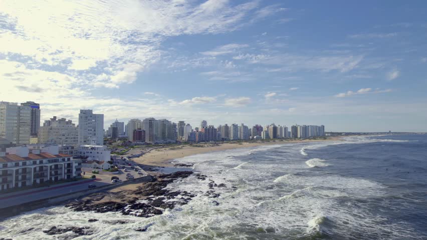 An aerial footage of El Emir beach and Brava Beach with the urban buildings in the background on a sunny day in Punta del Este city, Uruguay