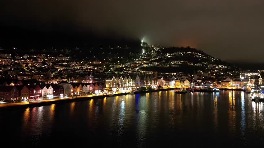 A drone hyperlapse flying on the riverfront to reveal the illuminated city center at night in Bergen, Norway