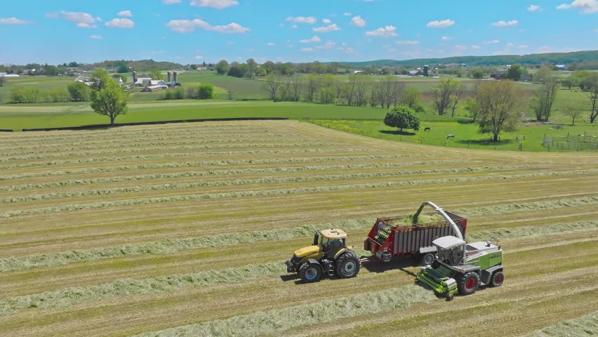 RONKS, US - May 06, 2023: An aerial drone shot of tractors working in harmony, baling hay as the day wanes, transforming fields into neatly organized lines, under azure skies.