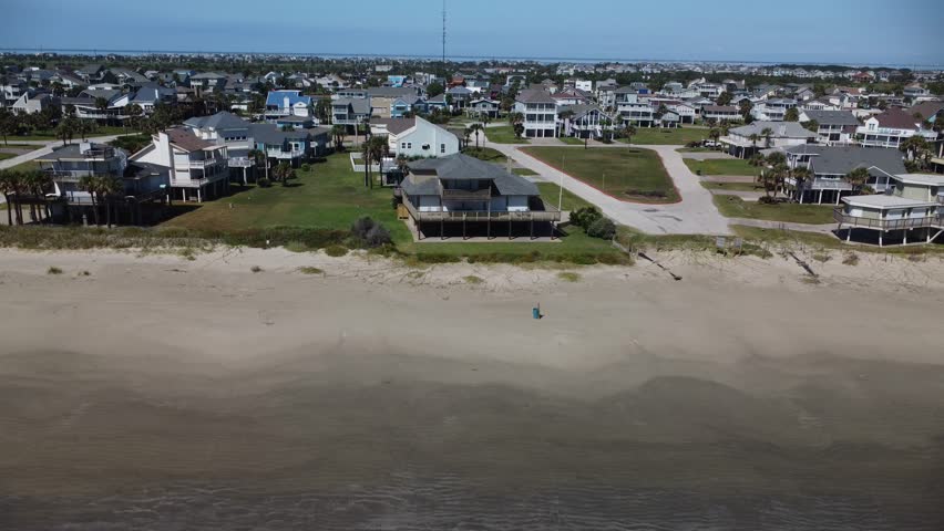 A receding drone shot of a scenic beach view of Galveston, Texas, showcasing the sandy shores and coastal neighborhoods.