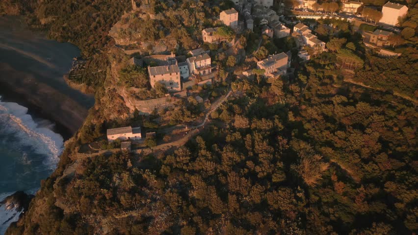 An aerial footage of the medieval Tower of Nonza and the nearby coastal buildings at sunrise in Nonza, Corsica island, France