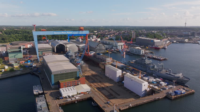Aerial views capture the Howaldtswerke Deutsche Werft shipyard in Kiel, Germany, showcasing German navy ships under construction, highlighting naval engineering and industrial activity