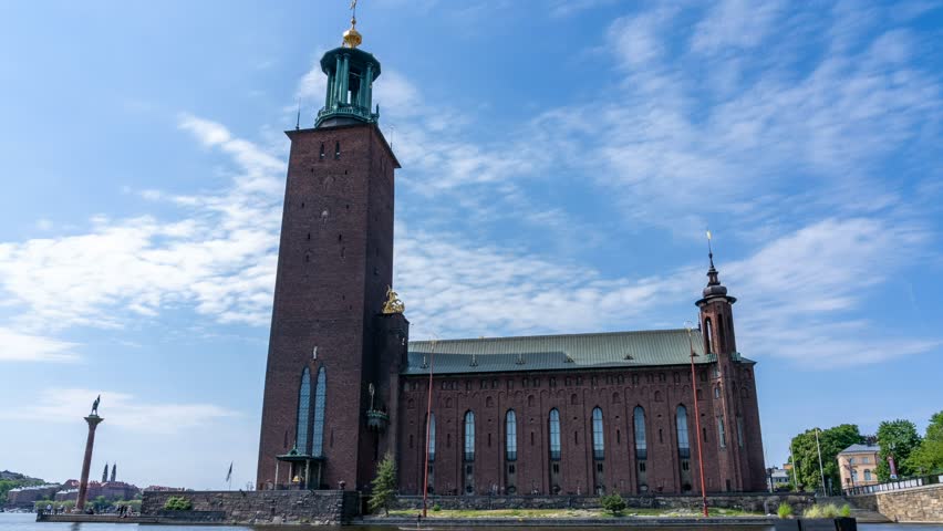 A timelapse of white clouds in sunny blue sky in the background of Stockholm City Hall in Stockholm, Sweden