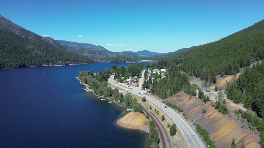 Aerial view of a beautiful lake surrounded by mountains and forest. Vehicles drive along the highway that follows the water