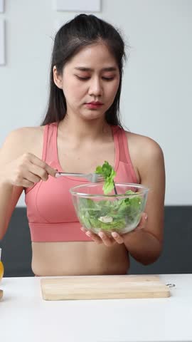 Beautiful healthy Asian woman happily eating delicious vegetable salad at home. Beautiful sport girl in sportswear enjoy eat clean vegetables after exercise for health in house. Diet and Healthy food.