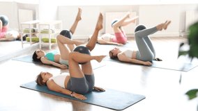 Slender young girls doing exercises in lying position holding softball between knees in pilates studio. High quality 4k footage - Powered by Shutterstock - Get 15% off with code: PIKWIZARD15