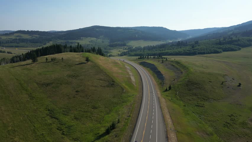 Scenic highway through rolling hills and green meadows. Cars drive along a winding road. Crowsnest Pass, Alberta, Canada.