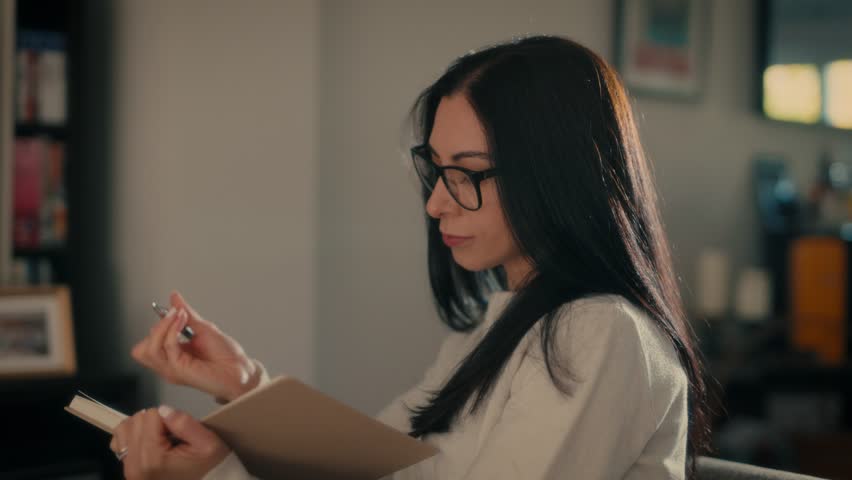 Attractive young woman writing notes on diary, notebook, making a plan lying on a sofa in a living room at home. Learning, Study, doing exams. Lifestyle Concept.