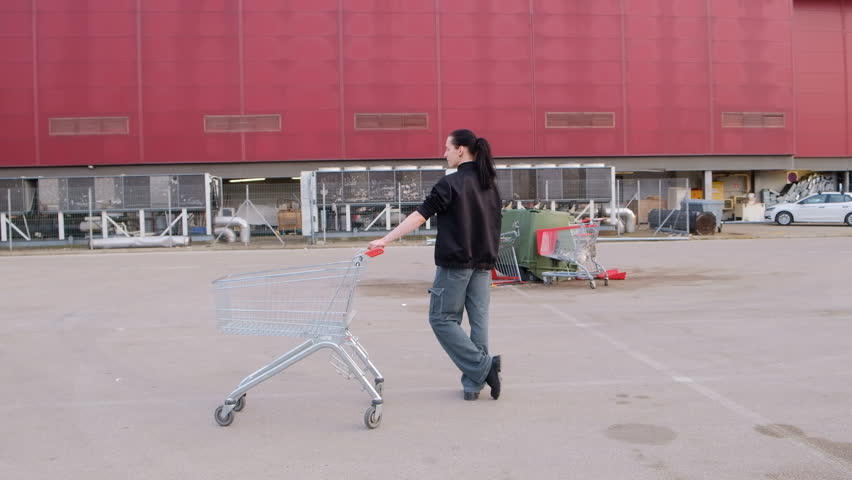 Young dancer by the shopping mall dances with a shopping cart on the parking lot