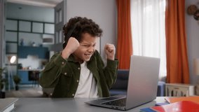 Funny little African American boy son kid child gamer at home table playing online video game internet gaming laptop computer win success winner victory wearing headphones achieve celebrate triumph - Powered by Shutterstock - Get 15% off with code: PIKWIZARD15