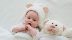 A cute newborn baby in a hat with a teddy bear lies on his back under a blanket before going to bed and sucks pens on a white bed in the bedroom, a happy cute baby, top view. High-quality 4k footage. - Powered by Shutterstock - Get 15% off with code: PIKWIZARD15