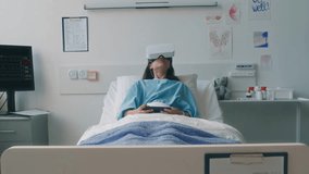 Full shot of little patient in augmented reality glasses lying in bed observing hospital ward in metaverse, holding mobile in hands during recovery period in modern clinic - Powered by Shutterstock - Get 15% off with code: PIKWIZARD15
