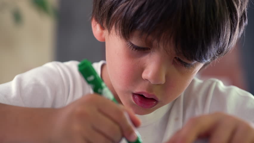 Boy coloring with a green marker, carefully drawing, highlighting his focus and engagement with the artistic process in a quiet home environment